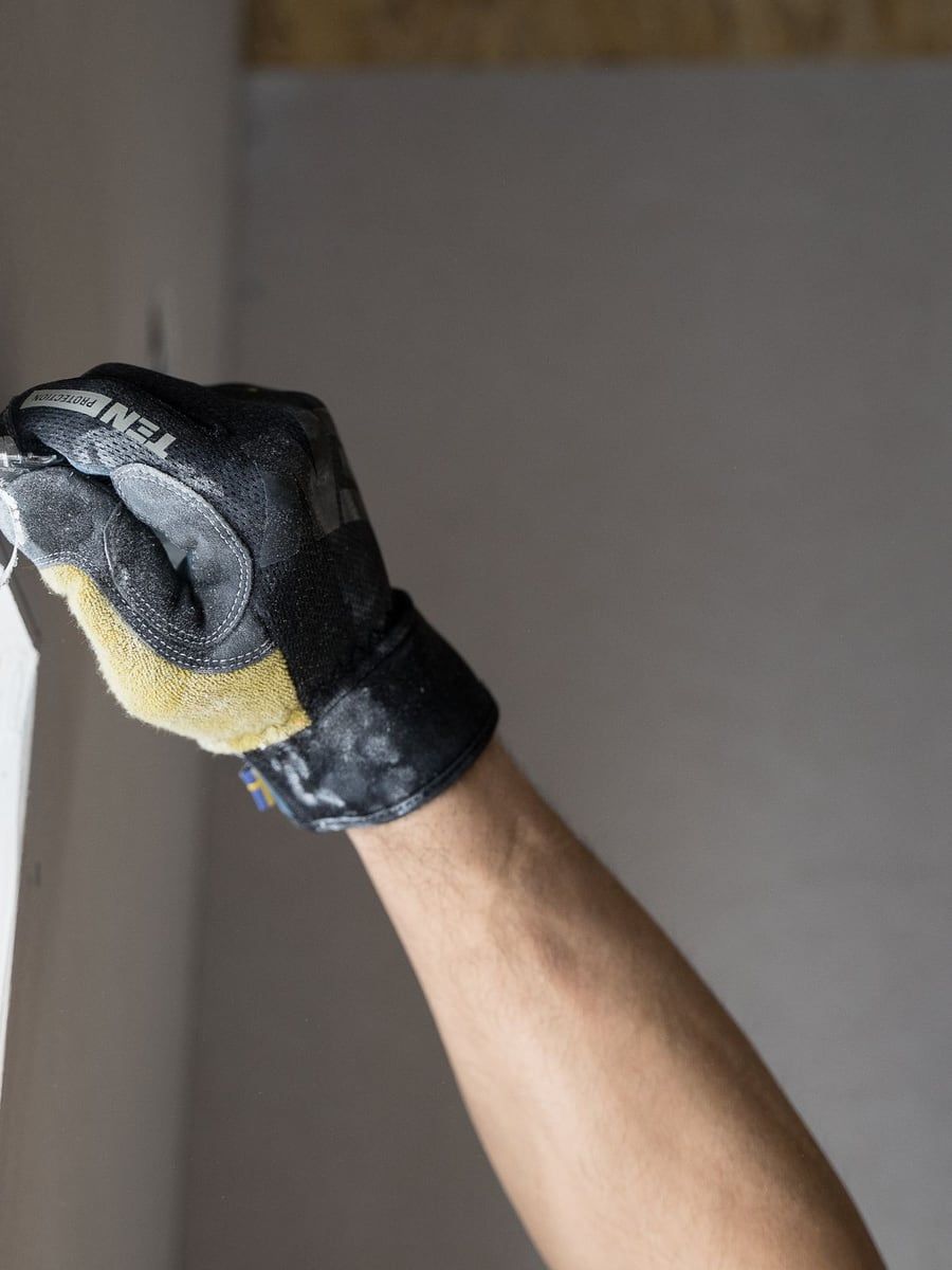 Behandschuhte Hand zieht Spachtelmasse über eine Wandfläche im Innenausbau