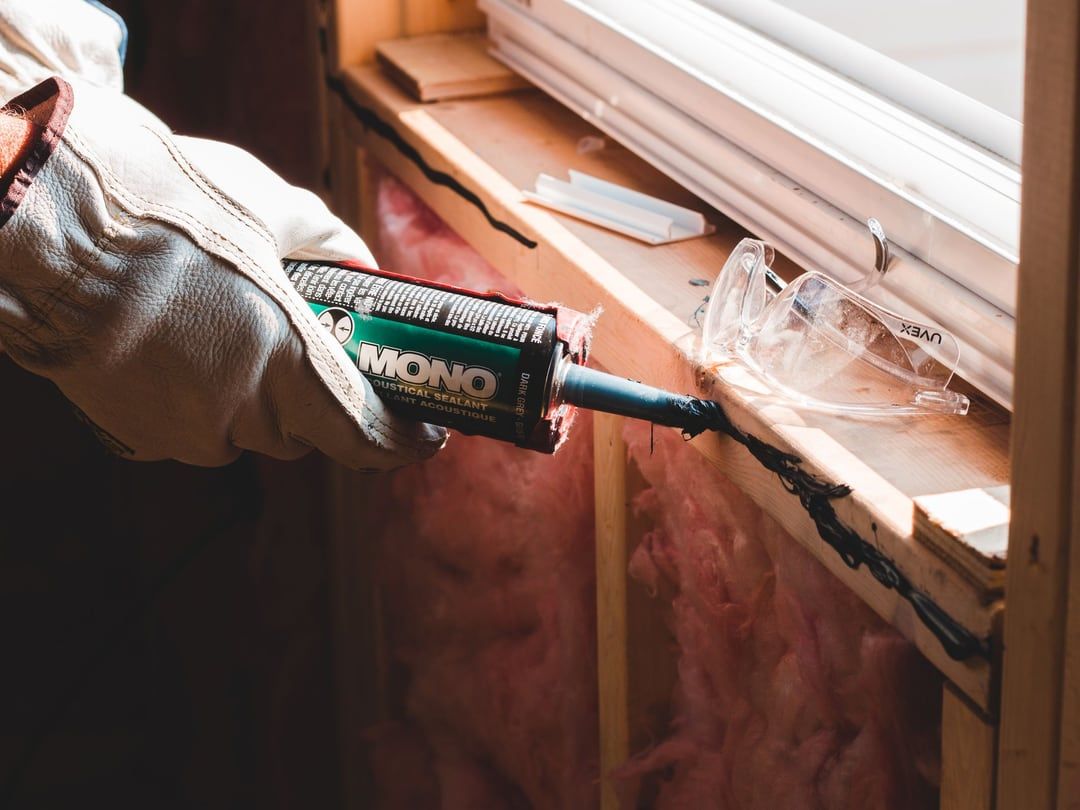 Behandschuhte Hand zieht eine Dichtstoffraupe entlang der Fuge eines eingebauten Fensters